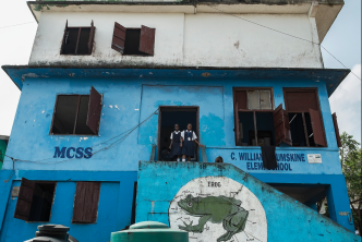 Photo of 3-storey blue Liberian school with two students in doorway