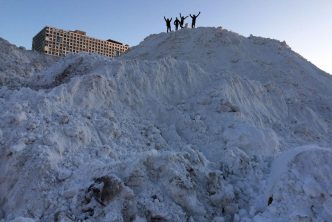 Students standing atop giant snow pile on west campus