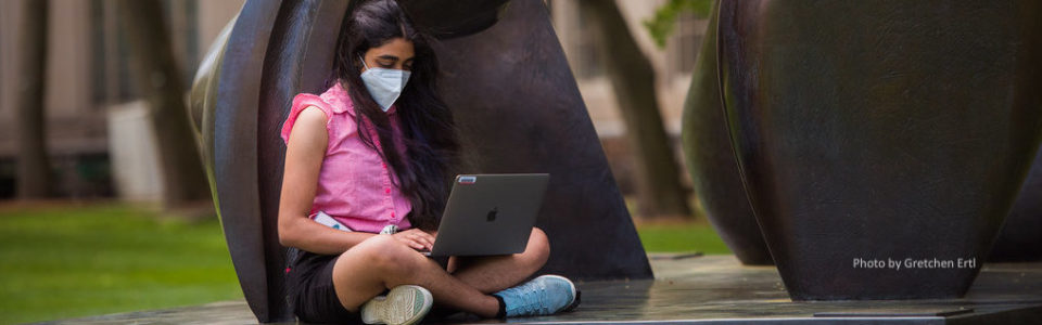 Masked student working on laptop outdoors