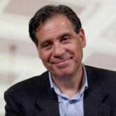 Andreas Karatsolis smiling. He is wearing a dark blue blazer and light blue collared shirt.